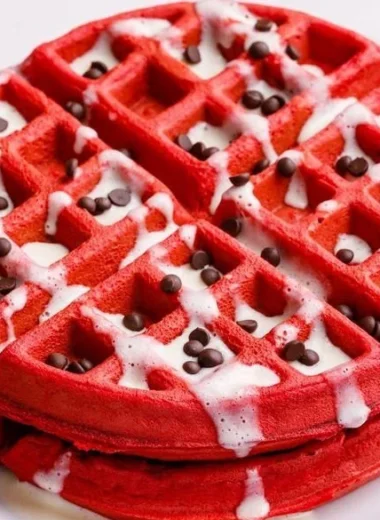 Delicious Red Velvet Waffles topped with cream cheese frosting and berries.