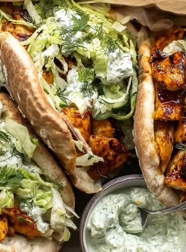 Sheet pan chicken pitas topped with herby ranch dressing on a wooden platter.
